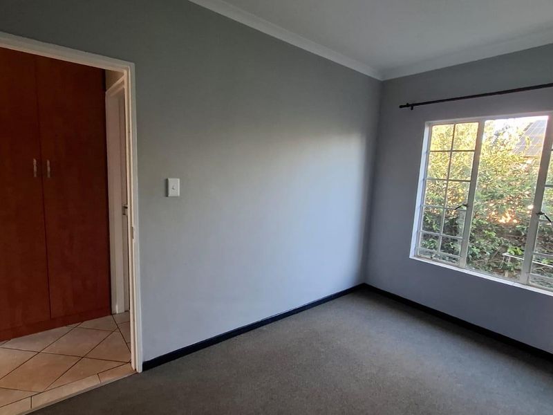 A vacant bedroom featuring grey walls, carpeted flooring, and built-in wooden cupboards, with natural light entering through a window with security bars.