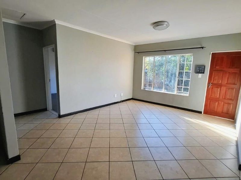 A spacious, empty living room featuring neutral wall tones, tiled flooring, and natural light through a large grid-pattern window.