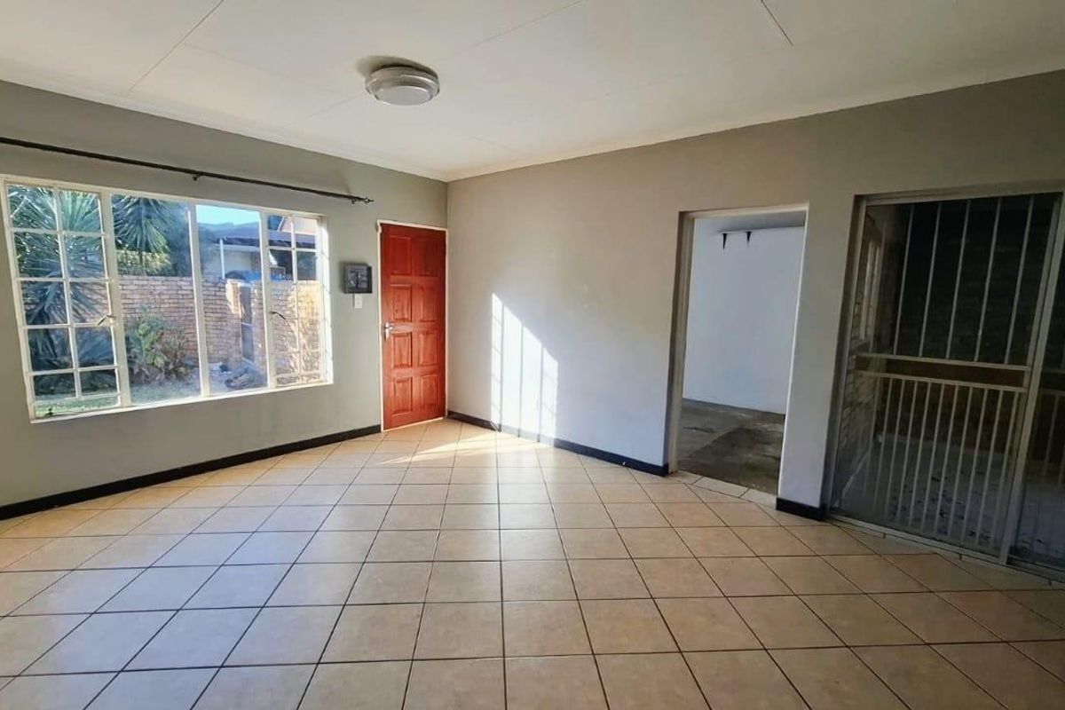 An empty, open-plan living area featuring neutral tiled flooring, a large window for natural light, and direct access to an adjacent space.