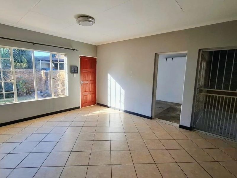 An empty, open-plan living area featuring neutral tiled flooring, a large window for natural light, and direct access to an adjacent space.