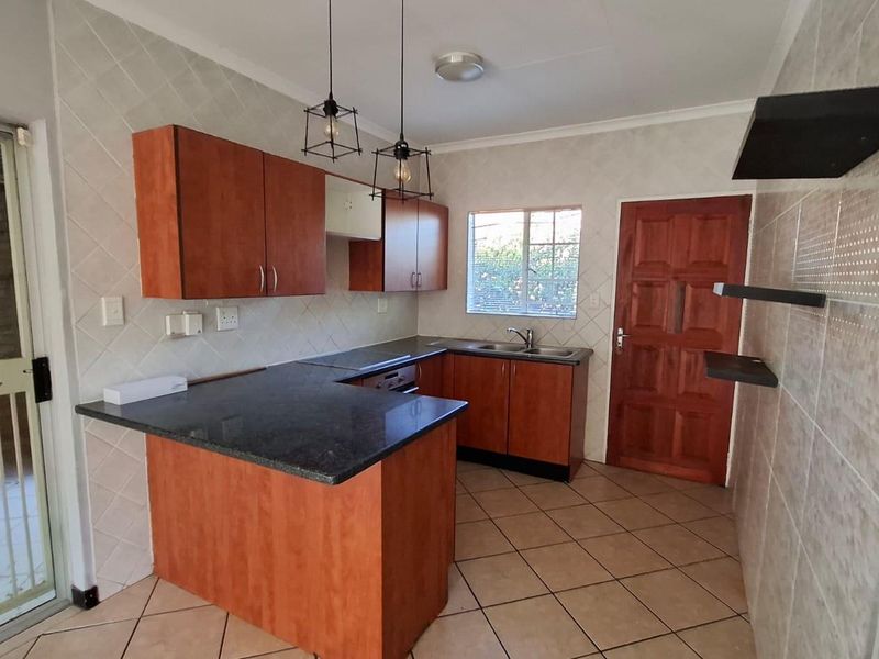 A functional kitchen featuring laminate cabinetry, granite countertops, tiled backsplash, and ceramic flooring, offering a practical layout with direct access to the exterior.