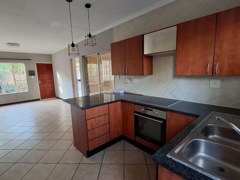 Open-plan kitchen and living area featuring tiled floors, wooden cabinetry, built-in oven and hob, and direct access to the outdoor patio area.