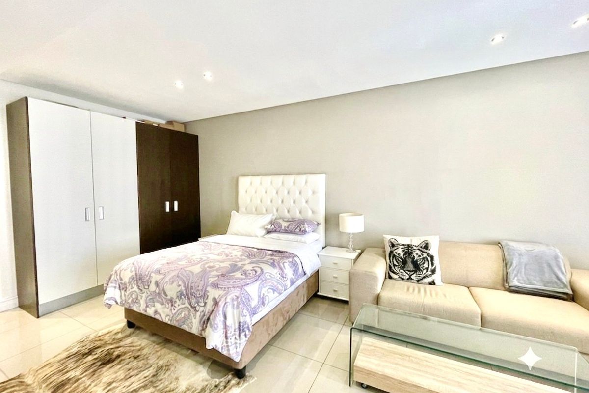 A spacious bedroom featuring neutral tiled flooring, recessed downlighting, and integrated built-in cupboards with a two-tone finish.
