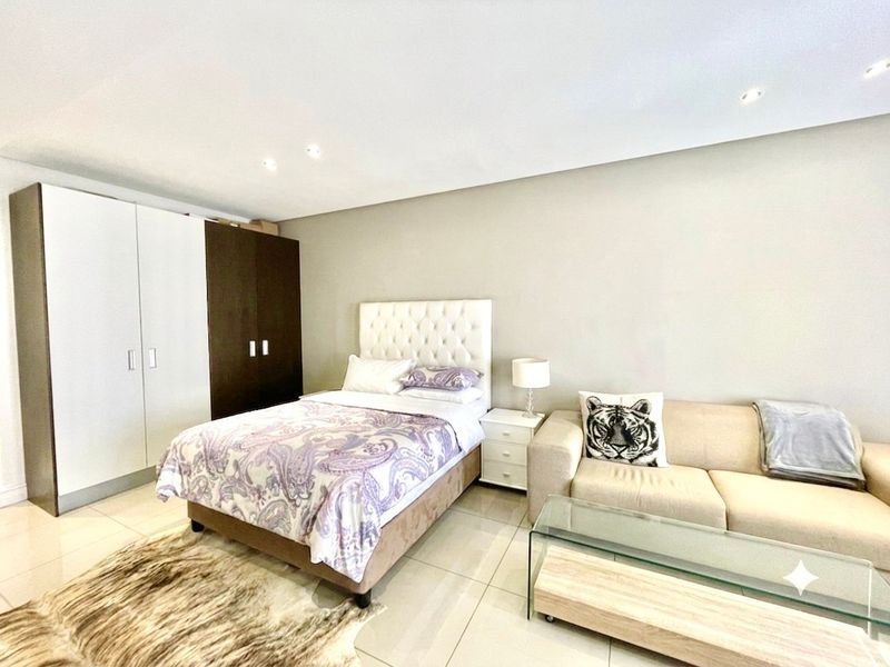 A spacious bedroom featuring neutral tiled flooring, recessed downlighting, and integrated built-in cupboards with a two-tone finish.