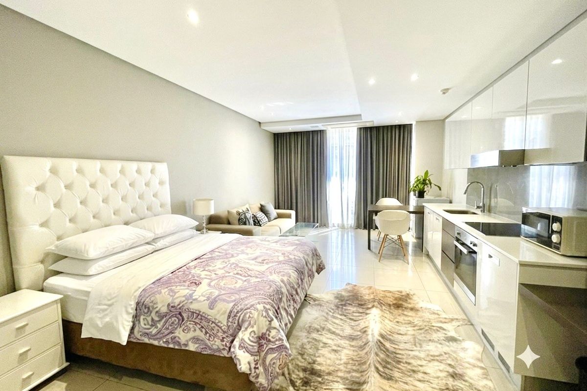 A modern open-plan studio apartment featuring a sleek kitchen with integrated appliances, tiled flooring, and recessed lighting, creating a functional and contemporary living space.