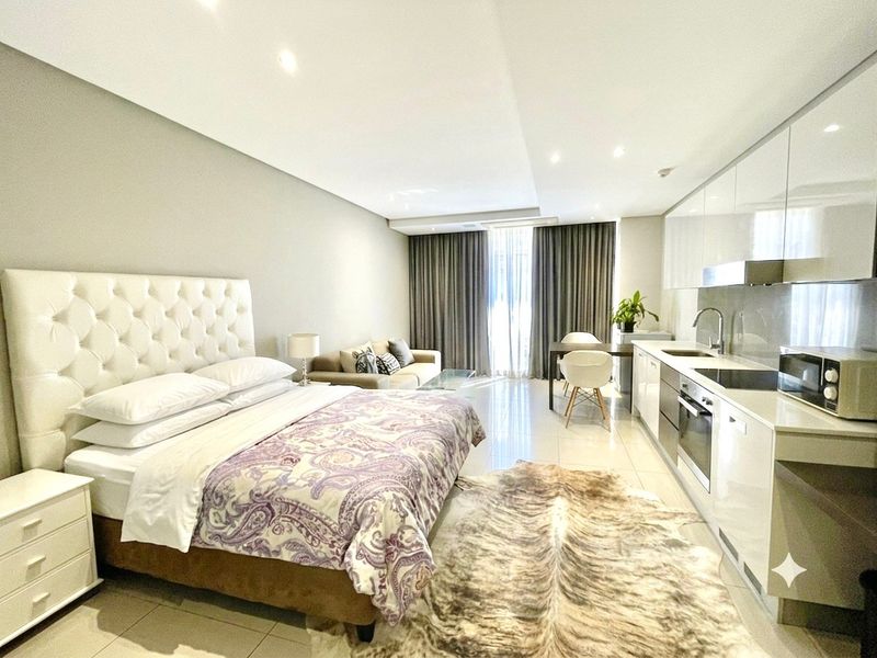 A modern open-plan studio apartment featuring a sleek kitchen with integrated appliances, tiled flooring, and recessed lighting, creating a functional and contemporary living space.