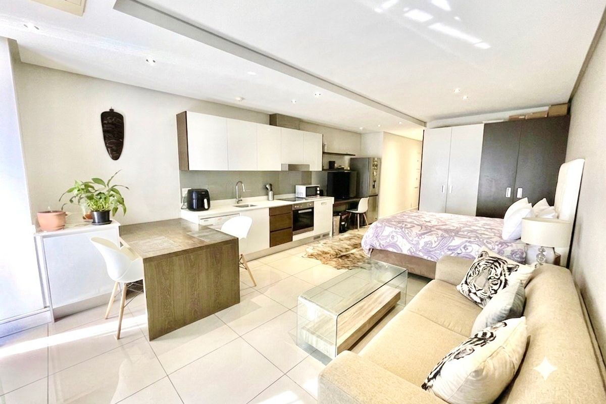A modern open-plan studio apartment featuring a sleek kitchen with built-in cabinetry, tiled flooring, and integrated storage solutions in a well-maintained living space.