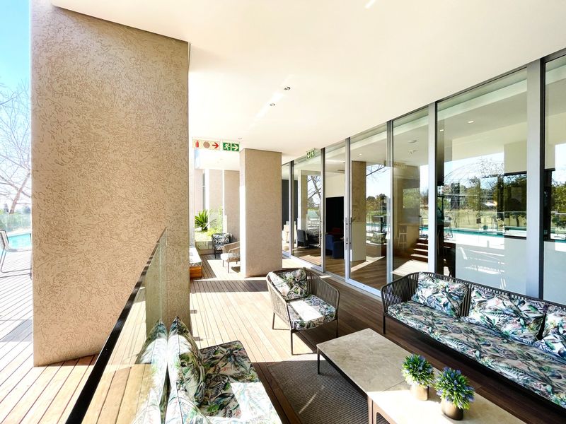 A spacious covered patio featuring timber decking, glass balustrades, and large sliding glass doors providing seamless indoor-outdoor flow.