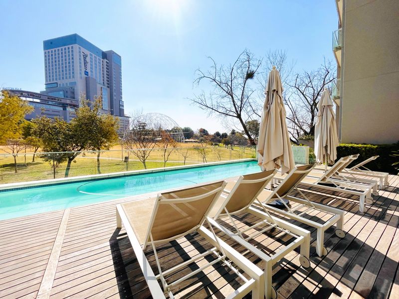Outdoor swimming pool area featuring timber decking, glass balustrades, and views of the surrounding urban landscape.