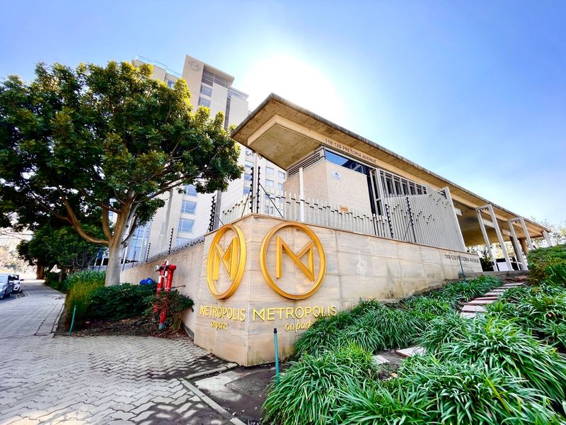 Exterior view of the Metropolis on Park apartment building, featuring modern stone cladding, prominent signage, and secure perimeter fencing.