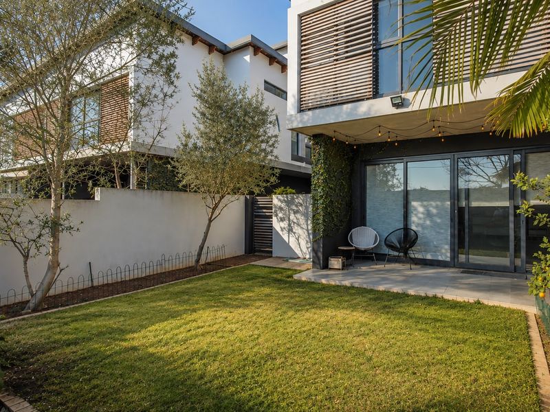 A well-maintained rear garden featuring a tiled patio, sliding glass doors, and modern architectural elements including timber louvre shutters.