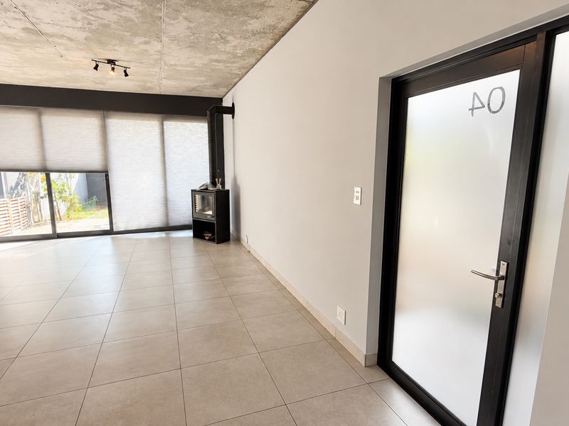 Spacious living area featuring an exposed concrete ceiling, large tiled floors, a modern freestanding fireplace, and direct access to the outdoor patio area.
