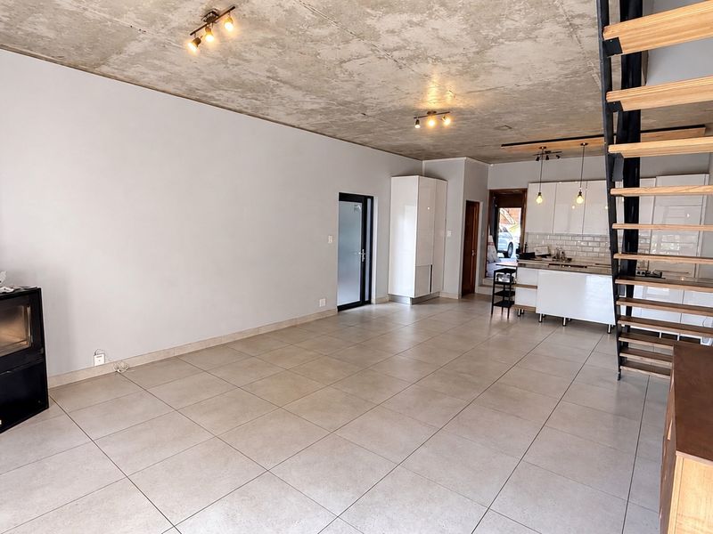 Spacious open-plan living area featuring an exposed concrete ceiling, tiled floors, a modern fireplace, and a striking staircase leading to the upper level.