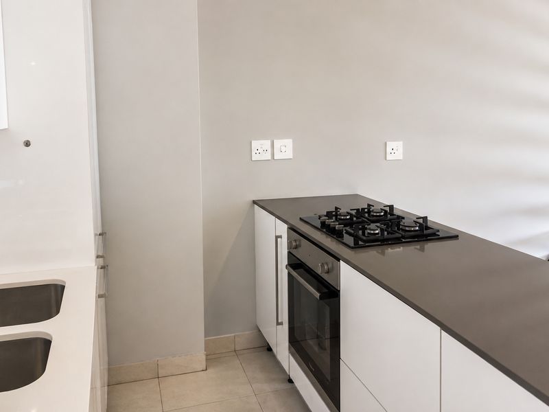 Modern kitchen featuring white cabinetry, stone countertops, a built-in oven, gas hob, and a double basin sink with a mixer tap.