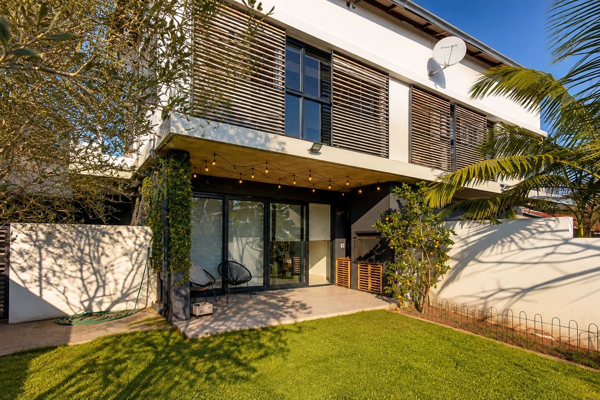 Rear exterior view of the townhouse featuring a paved patio, built-in braai area, sliding glass doors, and a private garden with timber privacy screens.