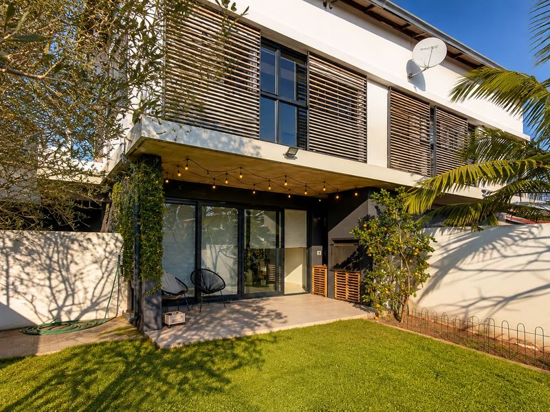 Rear exterior view of the townhouse featuring a paved patio, built-in braai area, sliding glass doors, and a private garden with timber privacy screens.