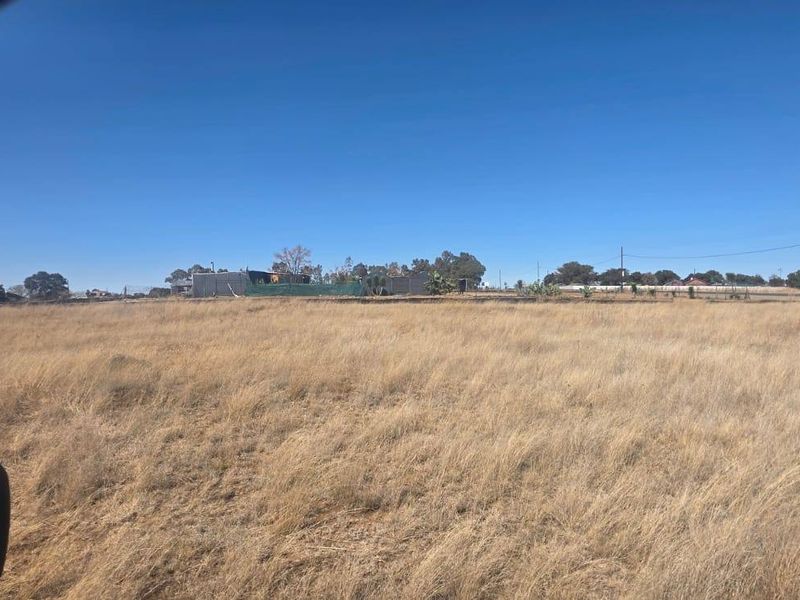 A wide-angle view of a vacant residential plot featuring dry grassland under a clear blue sky.