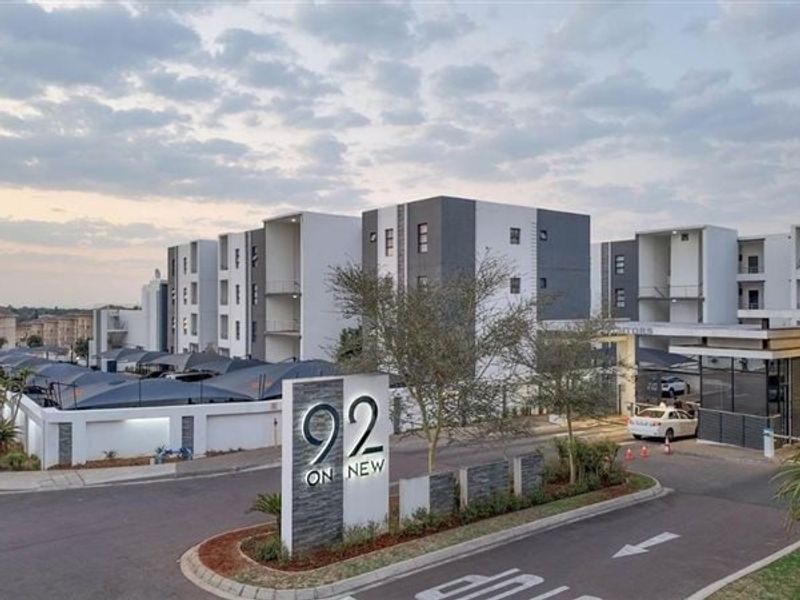 Exterior view of the 92 on New apartment complex, featuring a modern gated entrance, security gatehouse, and shaded parking facilities.
