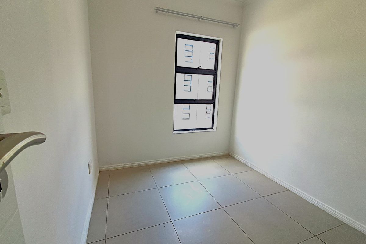 A clean, empty bedroom featuring neutral tiled flooring, white walls, and a single window with a fitted curtain rail.