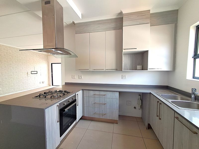 Modern kitchen featuring light wood-grain cabinetry, stone countertops, built-in oven, gas hob, stainless steel extractor fan, and a double bowl sink.