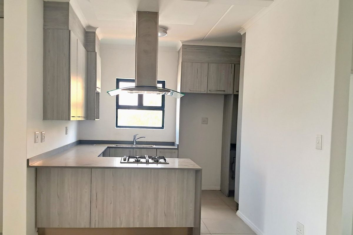 Modern kitchen featuring light wood-grain cabinetry, stone-look countertops, a gas hob with overhead extractor, and neutral tiled flooring in an open-plan layout.