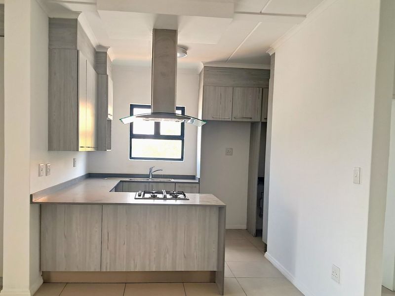 Modern kitchen featuring light wood-grain cabinetry, stone-look countertops, a gas hob with overhead extractor, and neutral tiled flooring in an open-plan layout.