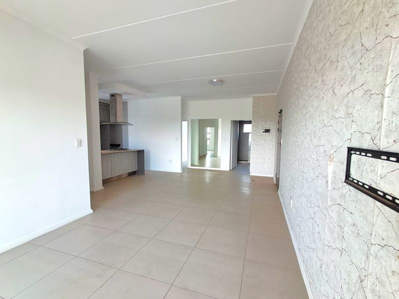 An open-plan living and kitchen area featuring tiled flooring, a modern kitchen layout with built-in appliances, and a feature wall with textured wallpaper.