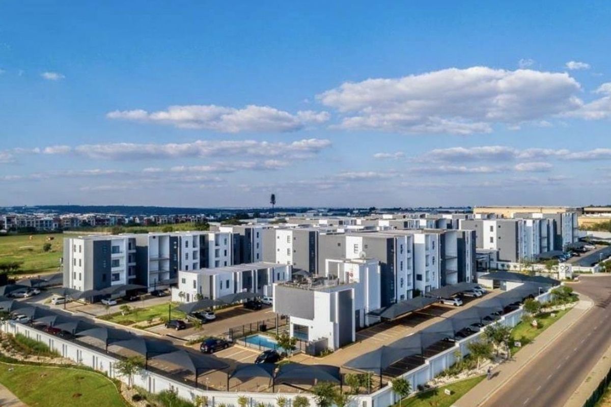Aerial view of a modern apartment complex featuring multiple residential blocks, covered parking bays, a communal swimming pool, and landscaped surroundings.