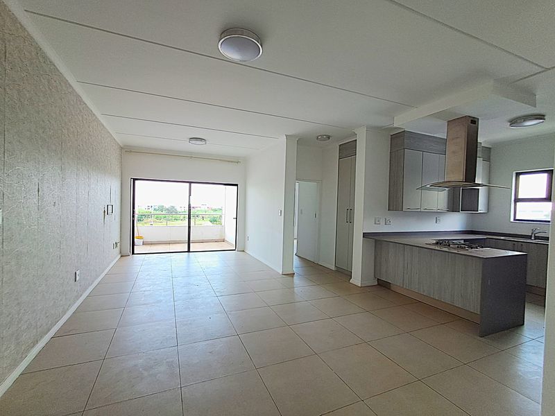 Spacious open-plan living area featuring tiled floors, a modern kitchen with built-in cabinetry, and a sliding door leading to a balcony.