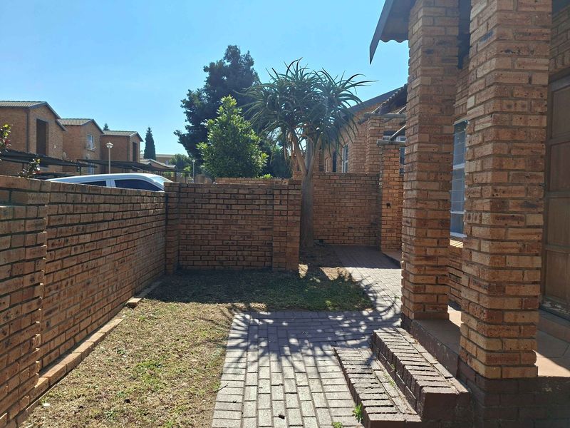 Front exterior view of a townhouse featuring a face brick facade, paved walkway, and a private garden area with a boundary wall.