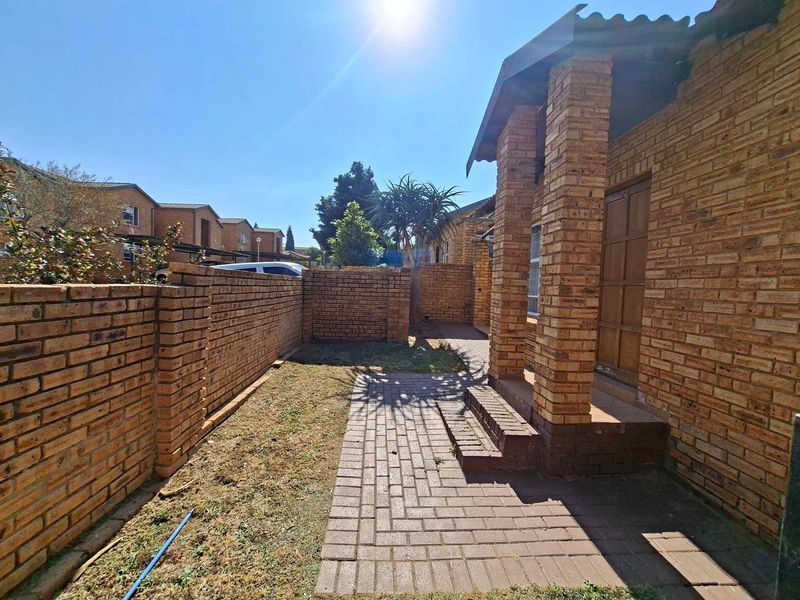 Front exterior view of a townhouse featuring a face brick facade, a paved entrance walkway, and a private enclosed garden area.