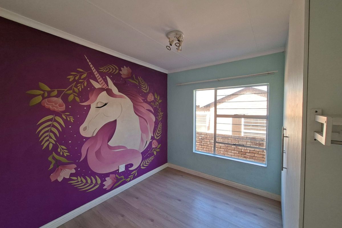 A bright bedroom featuring laminate flooring, a built-in wardrobe, and a decorative mural on the feature wall.