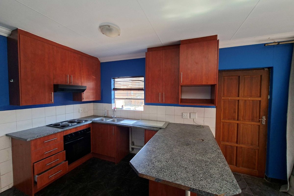 A functional kitchen featuring wood-finish cabinetry, granite-look laminate countertops, built-in oven and hob, and tiled flooring.