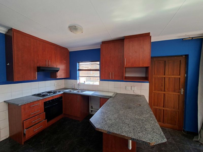 A functional kitchen featuring wood-finish cabinetry, granite-look laminate countertops, built-in oven and hob, and tiled flooring.