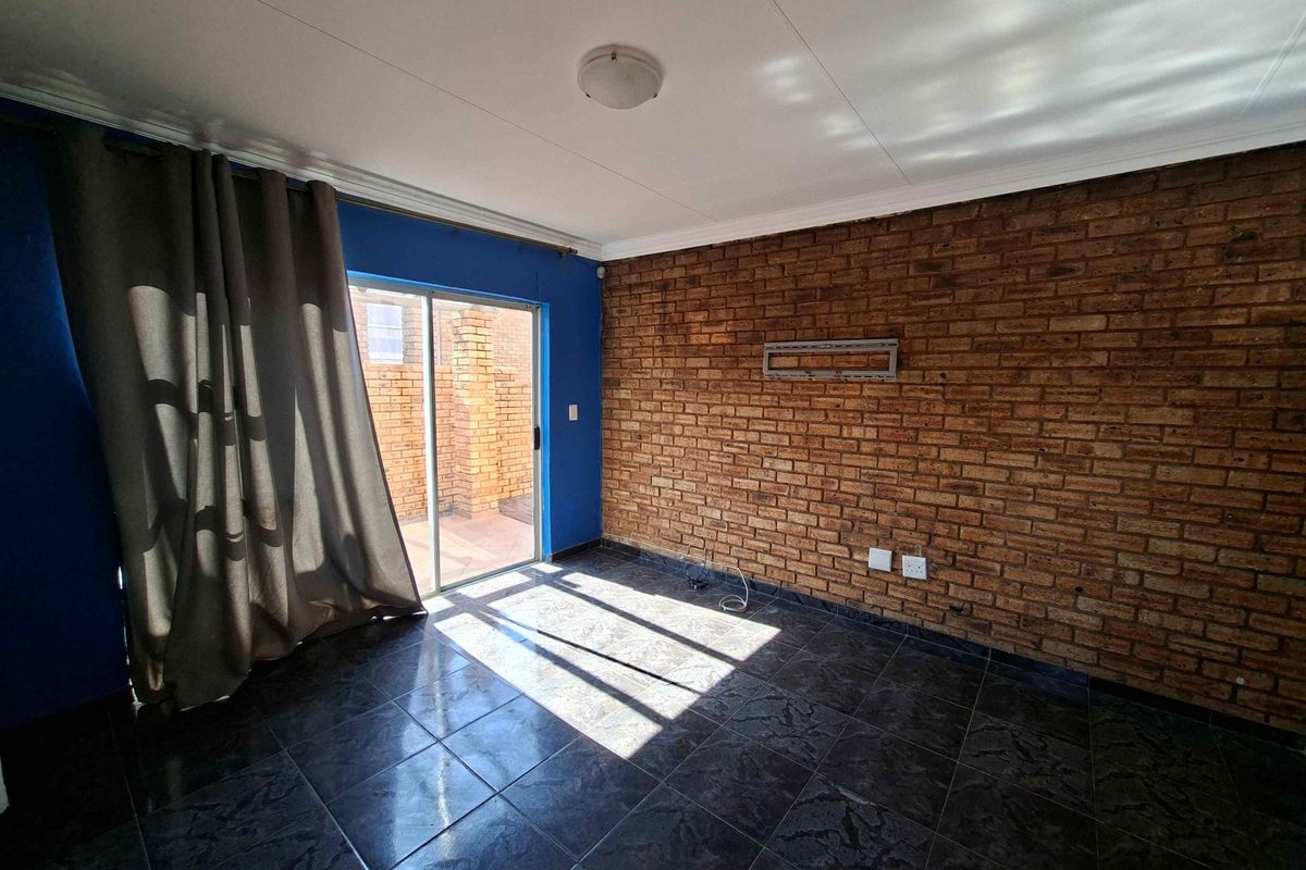 An empty living room featuring an exposed brick wall, dark tiled flooring, and a sliding glass door providing access to the outdoor area.
