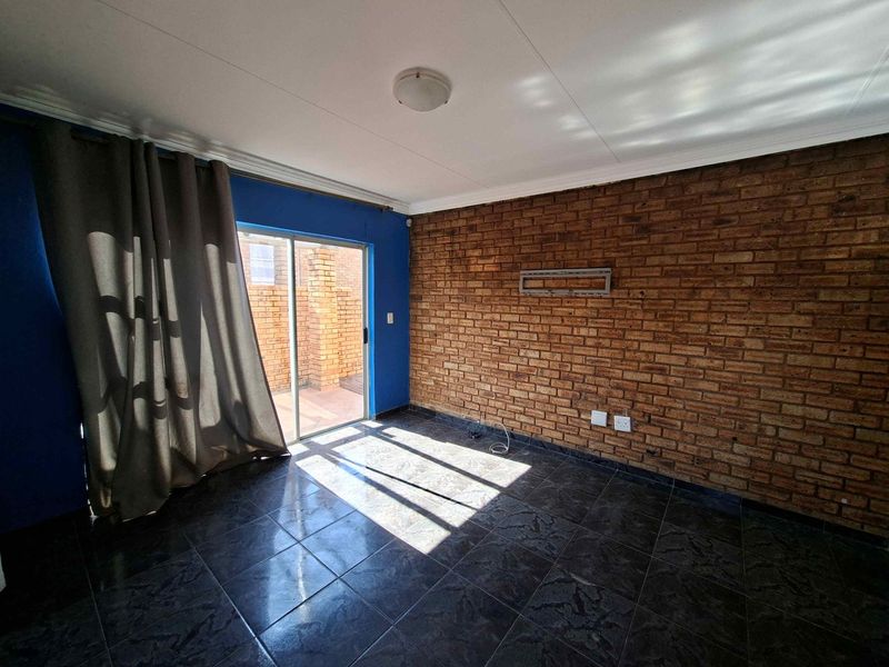 An empty living room featuring an exposed brick wall, dark tiled flooring, and a sliding glass door providing access to the outdoor area.