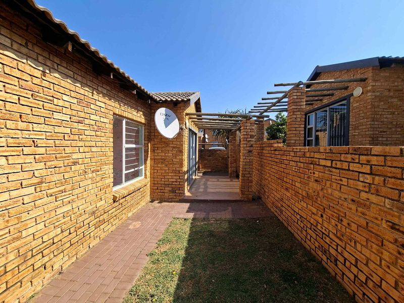 Rear exterior view of a townhouse featuring face brick walls, a paved walkway, and a timber pergola structure.