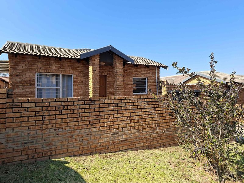 Front view of a face-brick townhouse featuring a tiled roof, aluminium window frames, and a private brick boundary wall with a small garden area.