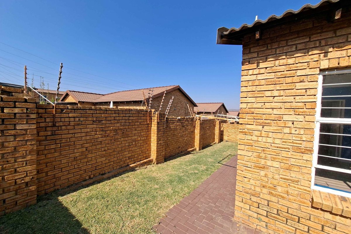 A private rear garden area featuring a paved walkway, face brick boundary walls with electric fencing, and a tiled roof structure.
