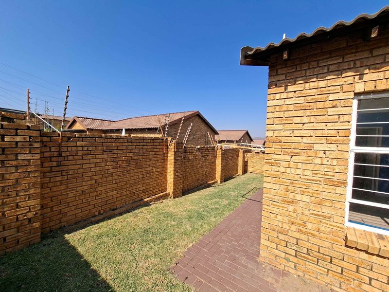A private rear garden area featuring a paved walkway, face brick boundary walls with electric fencing, and a tiled roof structure.