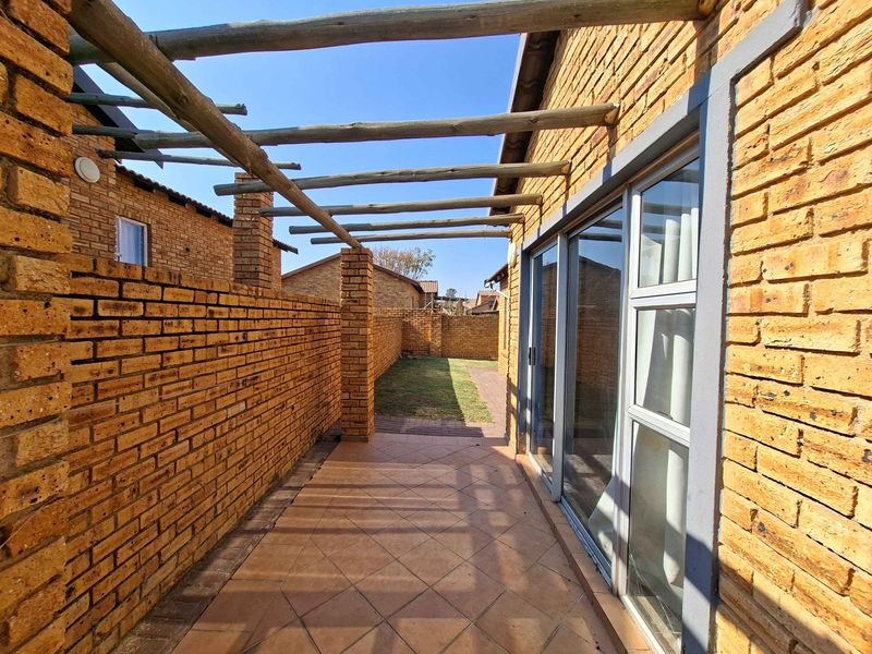 A private outdoor patio area featuring a timber pergola, tiled flooring, and sliding glass door access to the interior living space.