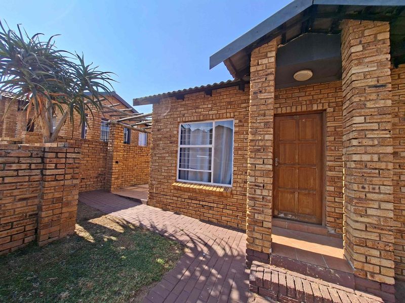 A charming face-brick townhouse exterior featuring a paved walkway leading to a covered entrance porch and a classic timber front door.