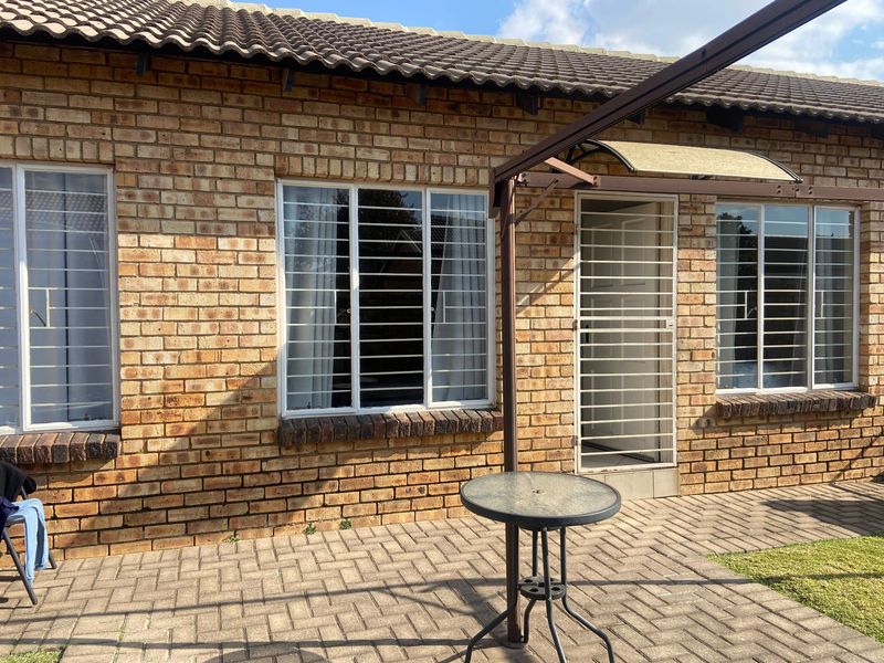 Rear exterior view of the townhouse featuring a face brick facade, tiled roof, security bars on windows, and a paved patio area.
