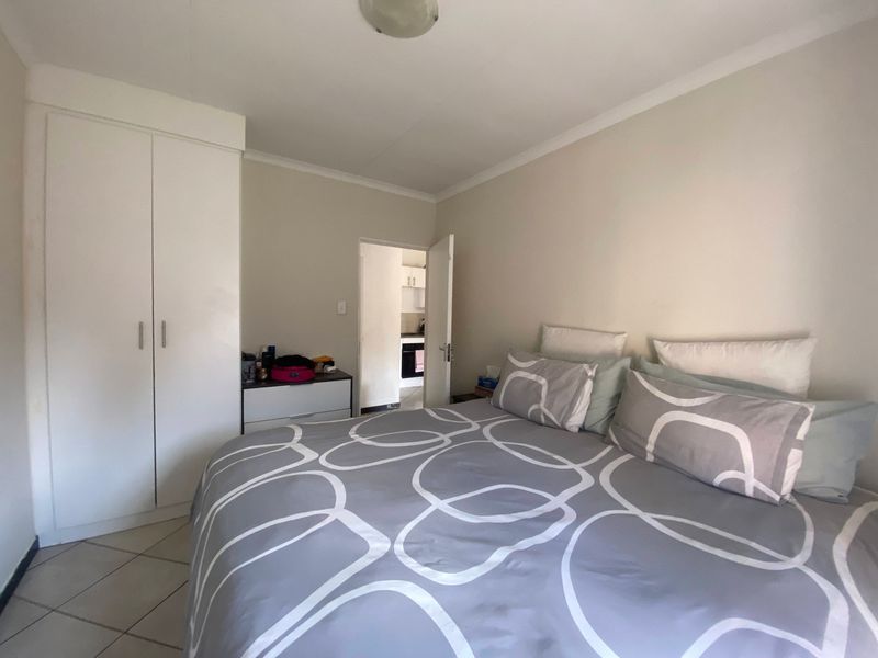 A functional bedroom featuring tiled flooring, a built-in wardrobe, and coved ceiling details, with direct access to an adjacent kitchen area.