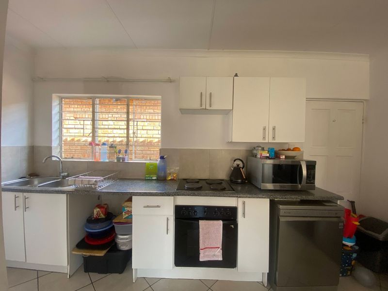 A functional kitchen featuring white cabinetry, a dark laminate countertop, built-in oven and hob, and tiled backsplash with a window overlooking the exterior.