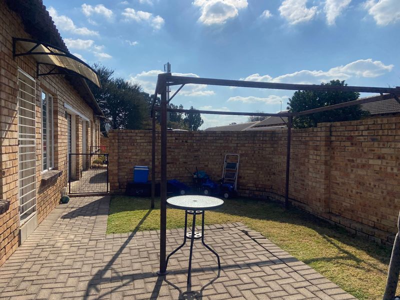 A private rear courtyard featuring a paved patio area, a brick boundary wall, and a metal pergola frame structure.