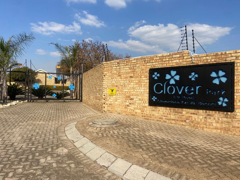 Entrance view of Clover Park complex featuring a brick boundary wall, electric fencing, and a secure metal gate access point.