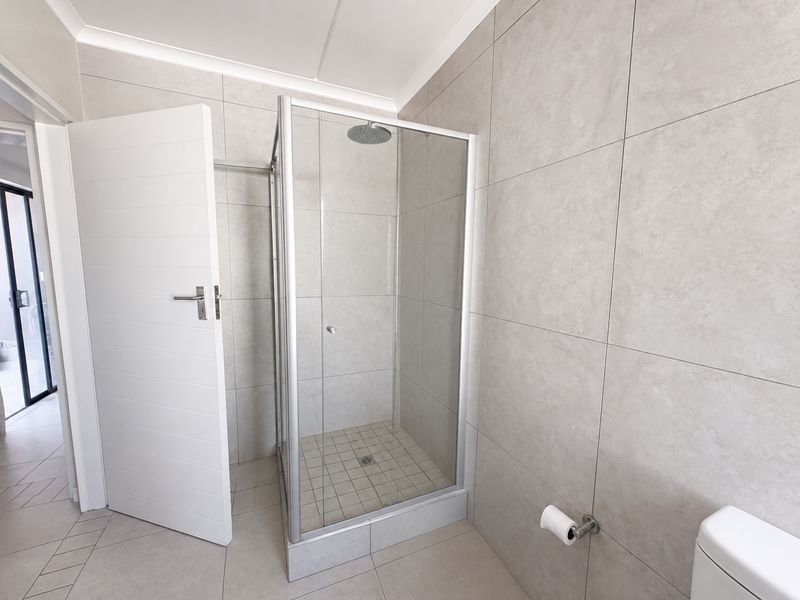 A clean, modern bathroom featuring a glass-enclosed shower with a rain shower head and neutral grey wall tiles.