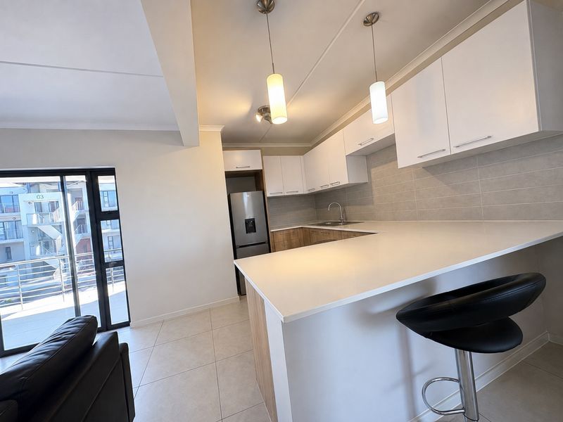 Modern open-plan kitchen featuring quartz countertops, sleek white cabinetry, tiled backsplash, and pendant lighting, seamlessly connected to the living area and balcony.