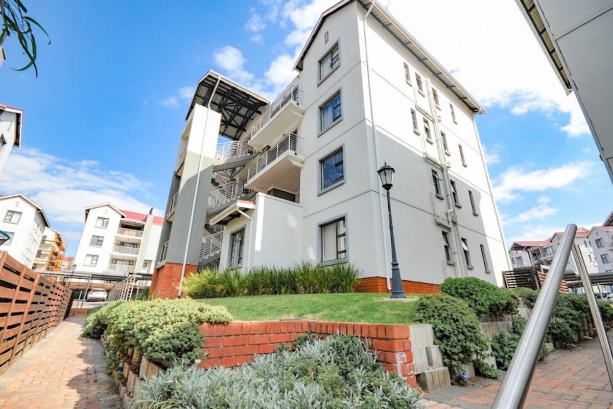 Exterior view of a multi-story apartment building featuring brick retaining walls, landscaped garden beds, and external metal staircases.